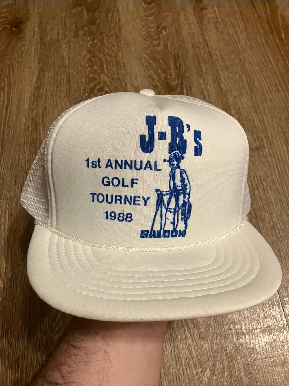 White trucker cap with blue graphic of a cowboy with the text 'J-R's 1st ANNUAL
